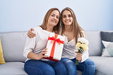 Two women mother and daughter surprise with birthday gift and flowers at home
