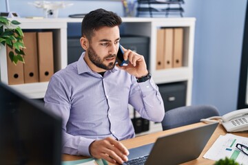 Young hispanic man business worker talking on the smartphone working at office