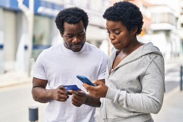 African american man and woman couple using smartphone and credit card at street