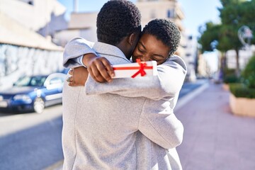 Man and woman couple hugging each other surprise with gift at street