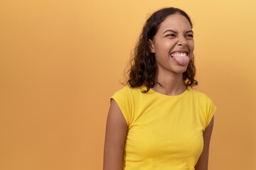 Young african american woman standing with tongue out over isolated yellow background