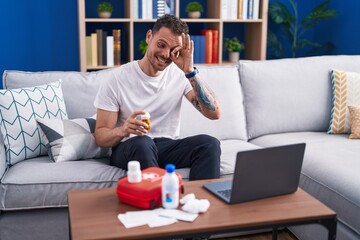 Young hispanic man watching video on laptop on how to use first aid kit smiling happy doing ok sign with hand on eye looking through fingers