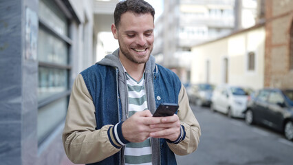 Young caucasian man smiling using smartphone at street