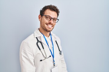 Young hispanic man wearing doctor uniform and stethoscope looking away to side with smile on face, natural expression. laughing confident.