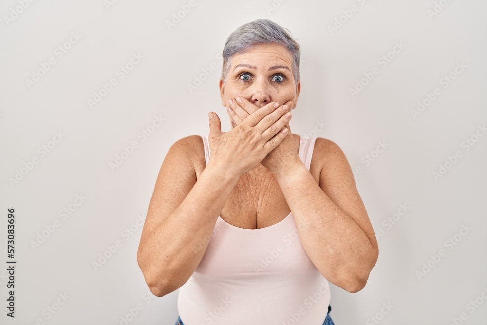 Sticker middle age caucasian woman standing over white background shocked covering mouth with hands for mist