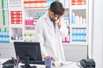 Fototapeta na wymiar Young arab man pharmacist using computer talking on telephone at pharmacy