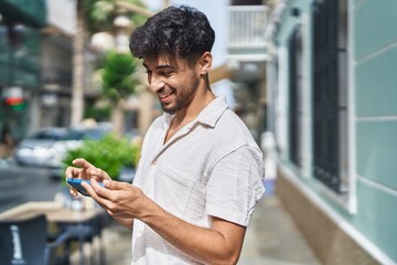 Young arab man smiling confident watching video on smartphone at street