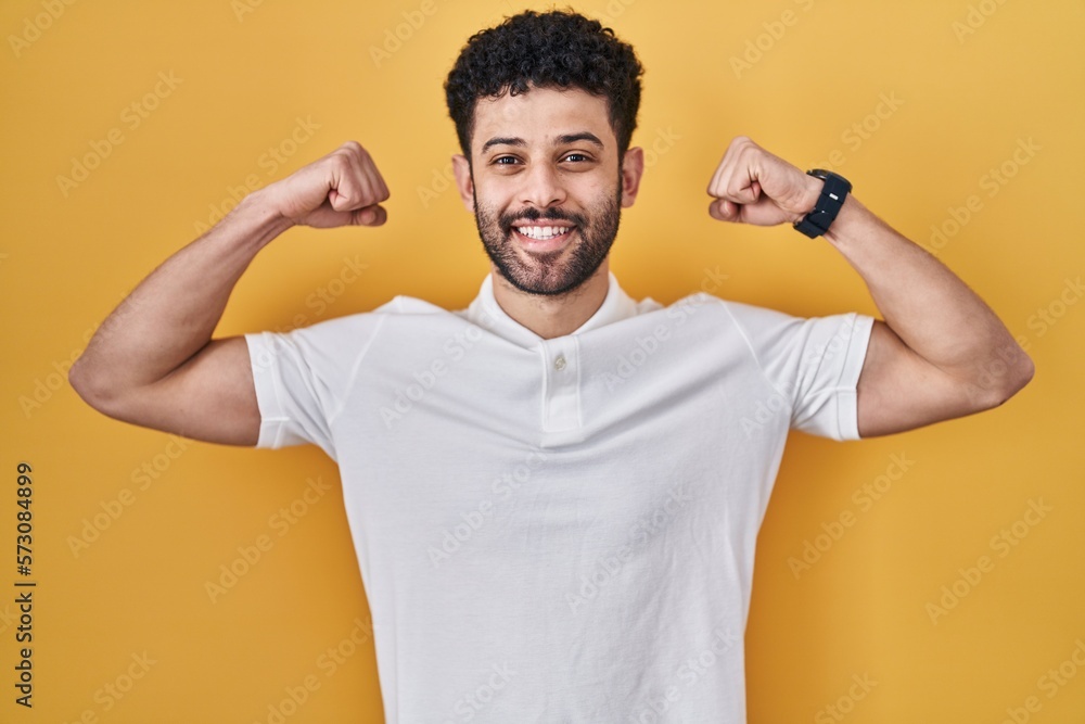 Poster arab man standing over yellow background showing arms muscles smiling proud. fitness concept.