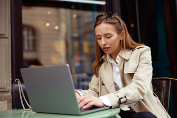 Attractive woman working on laptop online while sitting at outdoors cafe terrace. High quality photo