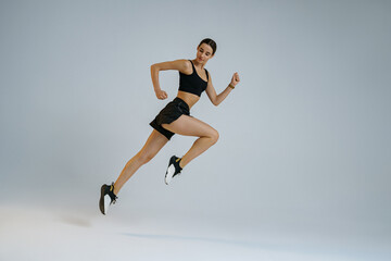 Athletic active woman wearing sportswear jumping on studio background. Dynamic movement