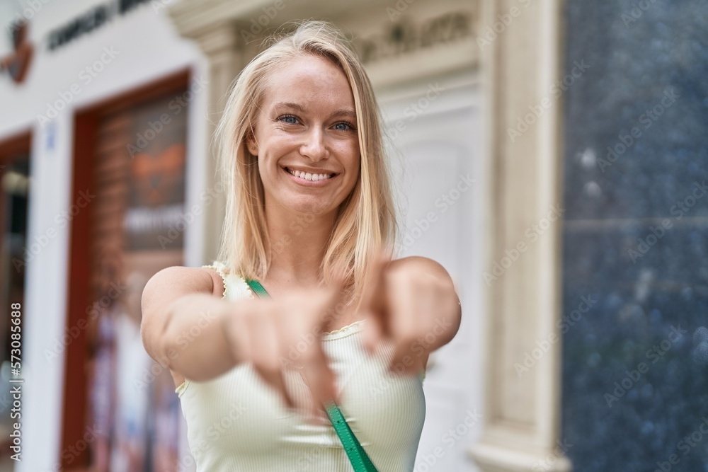 Wall mural Young blonde woman smiling confident pointing with fingers at street