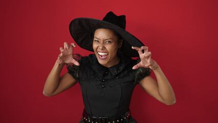 African american woman wearing witch costume doing scare gesture over isolated red background