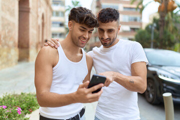 Two hispanic men couple smiling confident using smartphone at street