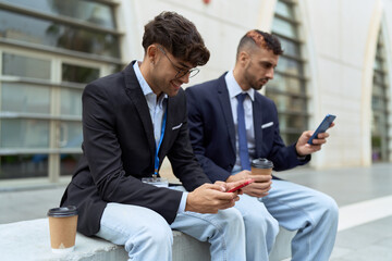 Two hispanic men business workers using smartphones drinking coffee at street