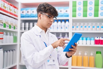 Young hispanic teenager pharmacist using touchpad working at pharmacy