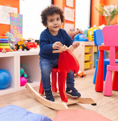 Adorable hispanic toddler smiling confident playing with reindeer rocking at kindergarten