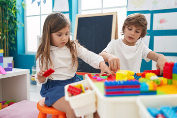 Brother and sister playing with construction blocks sitting on table at kindergarten