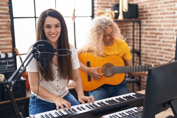 Two women musicians singing song playing classical guitar and piano at music studio