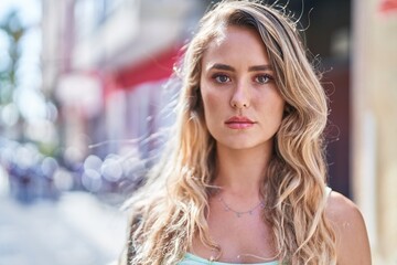 Young blonde woman standing with serious expression at street