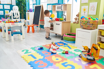 Adorable hispanic toddler playing with play kitchen standing at kindergarten