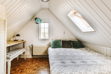 a bedroom with a bed, desk and window in the attic style dormer's loft at an old house