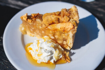 Apple pie slice dessert on a plate, apple slice with ice cream, whipped cream and caramel syrup on...