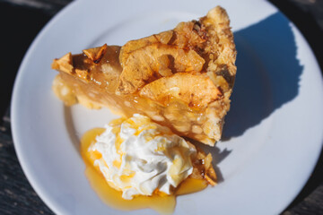 Apple pie slice dessert on a plate, apple slice with ice cream, whipped cream and caramel syrup on a white plate, traditional greek apple sweet pastry served in cafe of Corfu island, Kerkyra, Greece