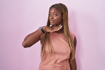 African american woman with braided hair standing over pink background cutting throat with hand as knife, threaten aggression with furious violence