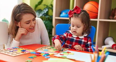 Teacher and toddler playing with maths puzzle game sitting on table at kindergarten