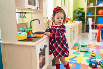 Adorable blonde toddler playing with play kitchen standing at kindergarten