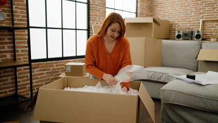 Young redhead woman smiling confident unpacking cardboard box at new home