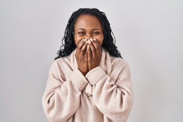 African woman standing over white background laughing and embarrassed giggle covering mouth with...