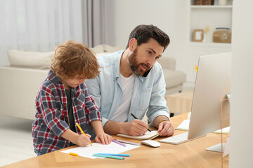 Man working remotely at home. Busy father talking on smartphone while his son drawing at desk