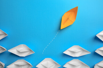 Yellow paper boat floating away from others on light blue background, flat lay. Uniqueness concept