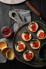 Delicious tartlets with red caviar and cream cheese served on wooden table, flat lay