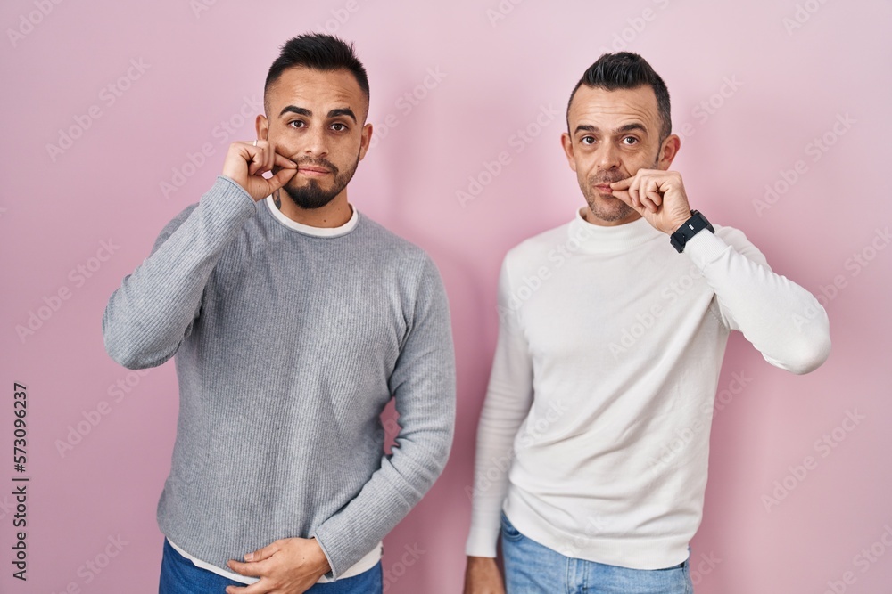 Poster Homosexual couple standing over pink background mouth and lips shut as zip with fingers. secret and silent, taboo talking