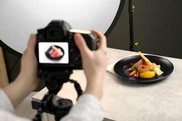 Woman taking picture of dish with chicken, parsnip and strawberries on grey table in professional photo studio, closeup. Food stylist