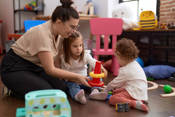 Teacher with girls playing with hoops toys sitting on floor at kindergarten