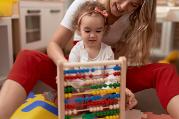 Teacher and toddler learning maths with abacus sitting on floor at kindergarten