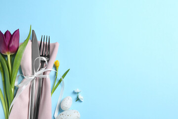 Cutlery set, Easter eggs and beautiful flowers on light blue background, flat lay with space for text. Festive table setting