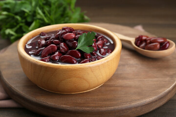 Bowl of canned red kidney beans with parsley on wooden table, closeup