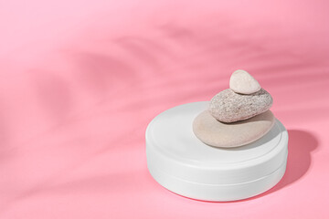 Fototapeta na wymiar Cosmetic product, stacked stones and shadow of tropical leaf on pink background. Space for text