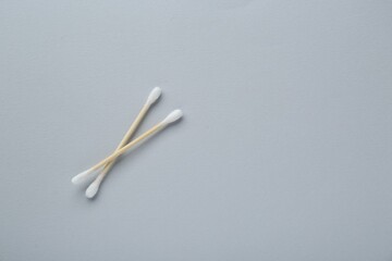 Two wooden cotton buds on light grey background, flat lay. Space for text