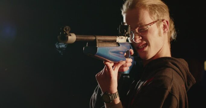 Air rifle being shot by a young man in a cinematically lit room
