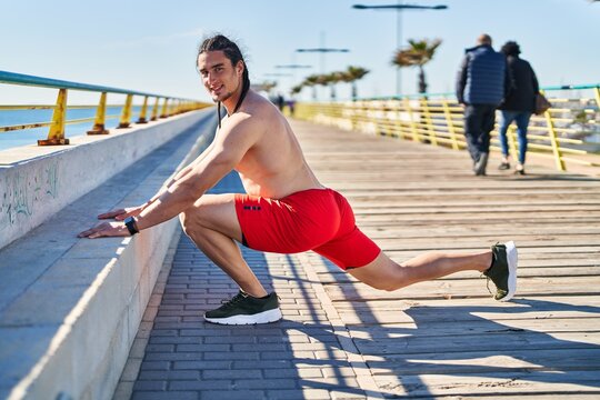 Young man smiling confident stretching legs at seaside