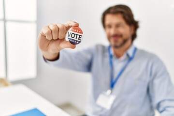 Middle age caucasian man smiling confident holding vote badge at electoral college