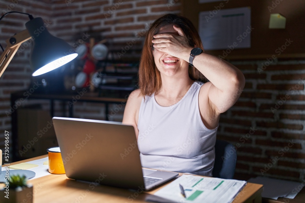 Sticker Brunette woman working at the office at night smiling and laughing with hand on face covering eyes for surprise. blind concept.