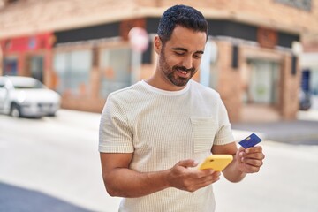 Young hispanic man using smartphone and credit card at street