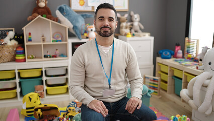 Young hispanic man preschool teacher smiling confident at kindergarten