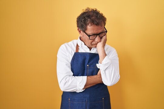 Middle age hispanic man wearing professional cook apron thinking looking tired and bored with depression problems with crossed arms.